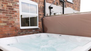 Een jacuzzi met bedieningspaneel, voor een bakstenen muur met een raam en een witte deur.