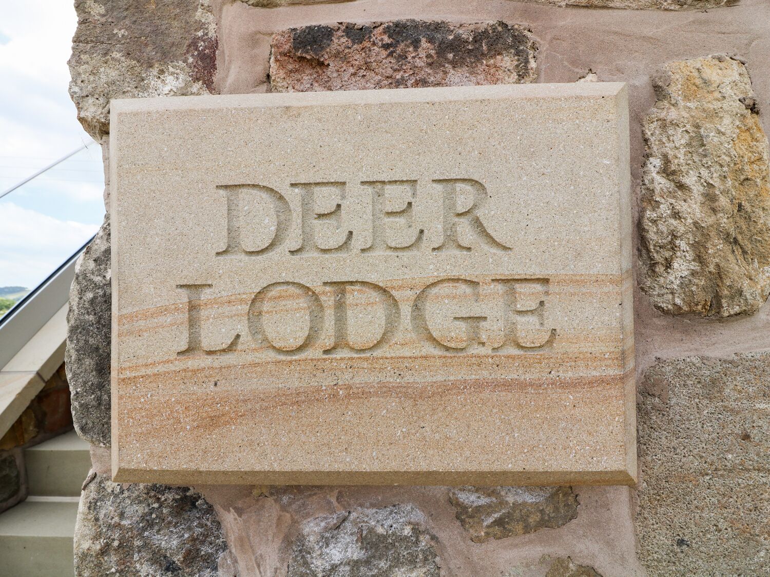 A stone sign with the inscription "DEER LODGE" on a building facade.