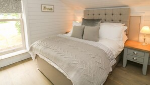 Un dormitorio con cama, mesita de noche, lámpara, ventana con cortinas e imagen enmarcada en la pared.