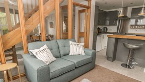 Ein modernes Wohnzimmer mit grauem Sofa, einer Holztreppe und einer Küchenzeile mit grauen Schränken und Edelstahlgeräten.