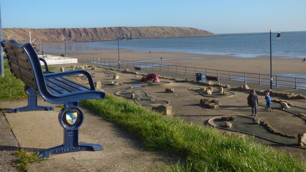 Eine Bank am Meer mit Blick auf Strand und Klippen.