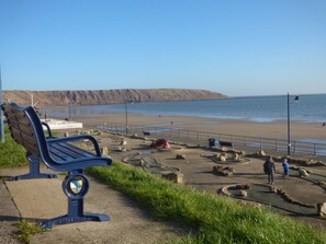 A bench by the seaside with a view of the beach and cliffs.