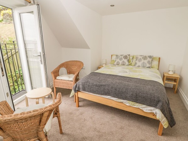 A bedroom with a bed, a chair, a small table, and a window with a view of greenery.