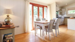 Una cocina acogedora con suelo de madera, una mesa de comedor con sillas, una lámpara de globo y un ventanal con cortinas.