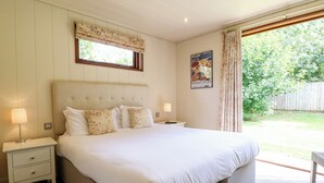Un dormitorio con una cama grande, dos mesitas de noche, un ventanal con cortinas florales, un cartel en la pared y vistas al exterior.