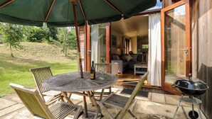 Un patio exterior con una mesa redonda, sillas, una parrilla y un paraguas grande.