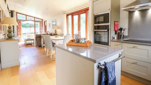Una cocina moderna con una isla central, hornos empotrados y un comedor con luz natural.