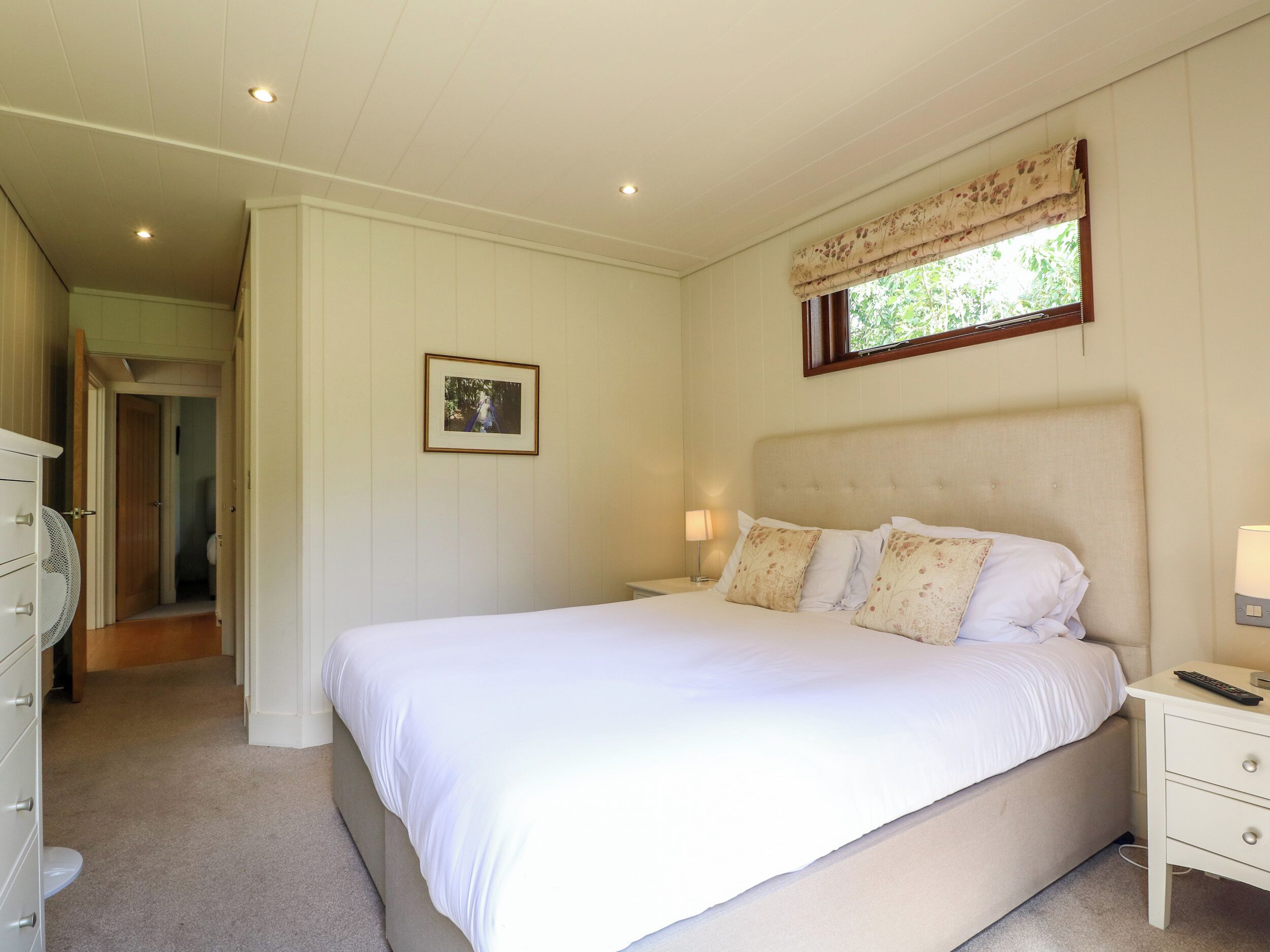 A bedroom with a large bed, a nightstand, a dresser, a framed picture on the wall, and a window with a valance.