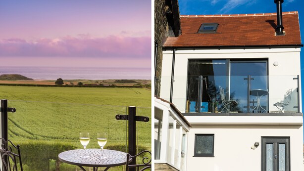 A terrace with a table and chairs, two glasses of wine, and a view of a green field. - Emblestones (Alnwick)