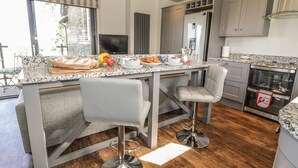 A modern kitchen with a marble countertop, two bar stools, a built-in oven, and a large window. - Emblestones (Alnwick)