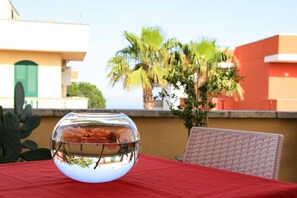 Un acuario sobre una mesa con mantel rojo, rodeado por un edificio con puerta verde y palmeras al fondo.