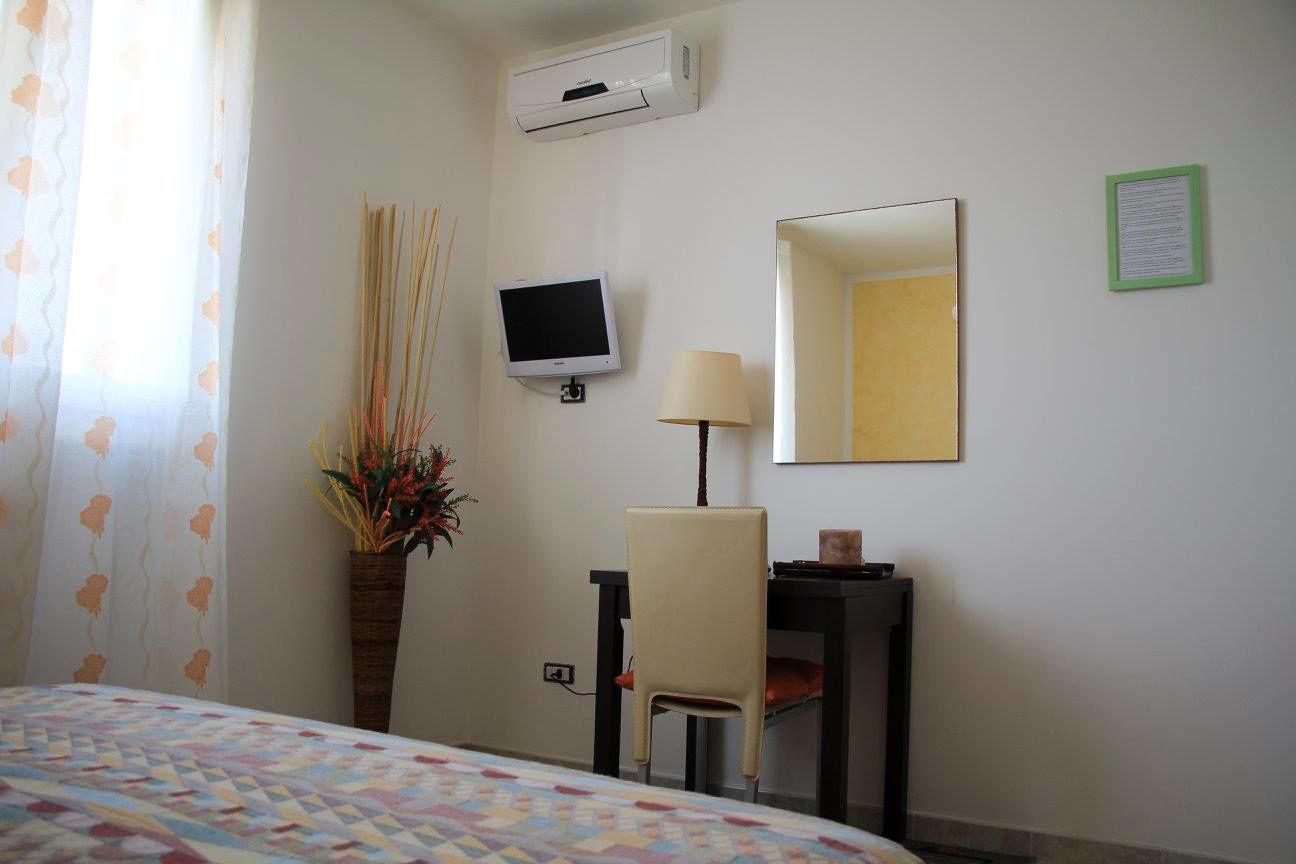 A hotel room with a bed, a desk with a chair, a television, a mirror, and a wall-mounted air conditioner.