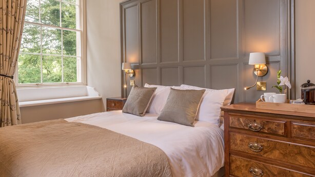 A bedroom with a large bed, two bedside lamps, a dresser with drawers, and a window with curtains. - Magistrates Chambers (Carnforth)