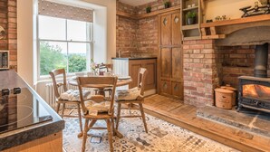 A cozy kitchen with a brick wall, wooden cabinets, a built-in wood stove, and a dining area with a table and chairs. - Magistrates Chambers (Carnforth)