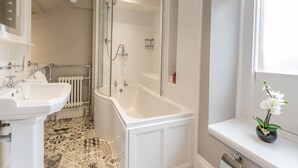 A bathroom with a white sink, a bathtub, and a shower. There is a window with a view of the outside. - Magistrates Chambers (Carnforth)