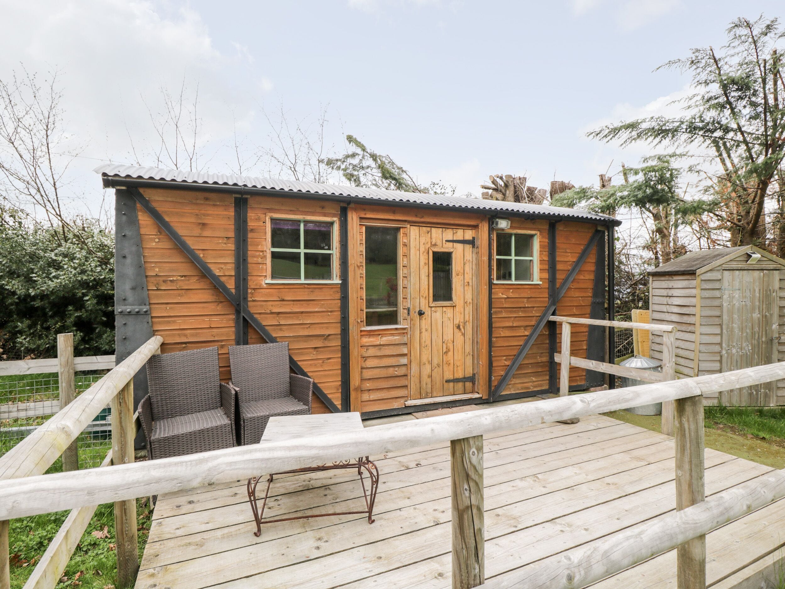 Een houten chalet met een deur, ramen en een klein terras met rieten meubels.