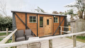 Een houten chalet met een deur, ramen en een klein terras met rieten meubels.