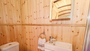 A wooden-paneled bathroom with a toilet, sink, and mirror. - Railway Carriage (Abergavenny)