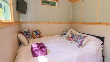 Un dormitorio con cama, almohadas, televisión y ventana.