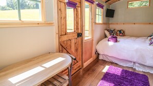 A cozy bedroom with a wooden door, a bed with white bedding, a purple rug, and a TV on the wall. - Railway Carriage (Abergavenny)