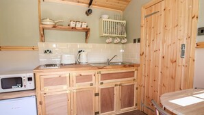 A compact kitchen with wooden cabinets, a microwave, a coffee maker, and a sink. - Railway Carriage (Abergavenny)