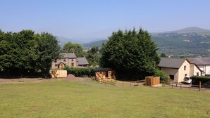 A rural landscape with a stone house, a wooden cabin, and a fenced area. - Railway Carriage (Abergavenny)