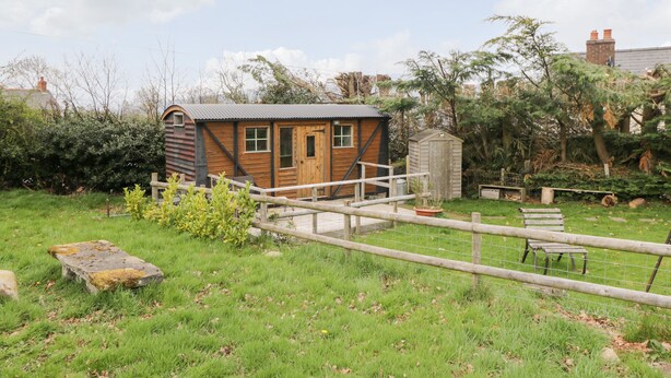 A small wooden cabin with a door and windows, surrounded by a grassy area and a wooden fence. - Railway Carriage (Abergavenny)