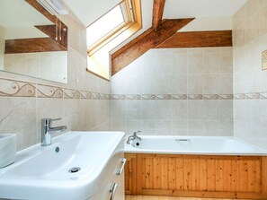 Un baño con una bañera de madera, un lavamanos blanco y un tragaluz.