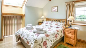 A bedroom with a bed, two bedside tables, a window with curtains, a wooden ceiling, and a skylight. - Y Bwthyn (Tywyn)