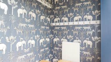 A room with a blue wall featuring a white animal and plant pattern. There is a white radiator and a wooden bench.