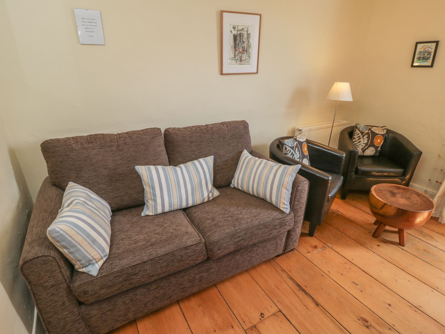 Un canapé marron avec des coussins à rayures, un fauteuil noir, une table basse en bois et un lampadaire.