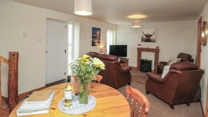 A living room with a wooden dining table, brown leather sofas, a television, and a fireplace.