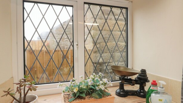 A kitchen with a window, a wooden planter with flowers, a scale, and a bottle of handwash.