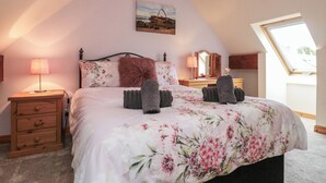 A bedroom with a sloped ceiling, a bed with floral bedding, two bedside lamps, a dresser, and a skylight.