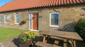 A stone building with a red-tiled roof, a wooden door, and a picnic table.