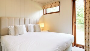 Una cama grande con muchas almohadas, una lámpara de noche y una ventana con cortinas.