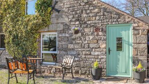 Una casa in pietra con una porta verde, una panchina e due sedie all'esterno.