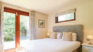 A bedroom with a large bed, a nightstand, a window with curtains, and a framed picture on the wall. - Brooke (Oakham)