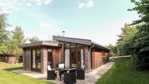 A modern house with a patio, large windows, and a lawn. - Brooke (Oakham)