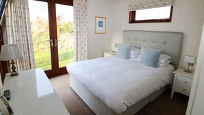 Quarto com uma cama grande, duas mesas de cabeceira com abajures, uma escrivaninha com luminária e uma janela com cortinas.