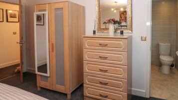 A bedroom with a bed, a wooden wardrobe, a dresser, a mirror, and a bathroom visible through an open door.