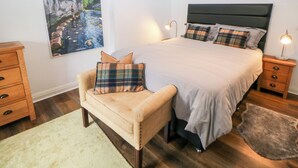 Une chambre à coucher avec un lit, une chaise, une table de chevet, une lampe et un tableau au mur.