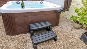 A hot tub with a wooden bench and a step, surrounded by pebbles.