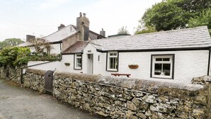 A stone wall with a gate, a white building with a tiled roof, and a bench outside. - Ty Coed (Caernarfon)
