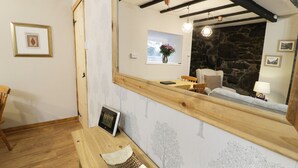 A cozy room with a wooden bench, a small table, and a mirror reflecting a stone wall and a window with flowers. - Ty Coed (Caernarfon)
