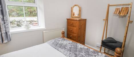 A bedroom with a bed, a wooden dresser, a mirror, a wooden chair, and a window with curtains.