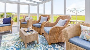 A sunroom with wicker furniture, large windows, and a view of the countryside. - Penhallick House (Tintagel)