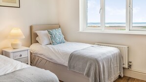 A bedroom with a bed, a nightstand, a lamp, a window with a view, and a framed picture on the wall. - Penhallick House (Tintagel)