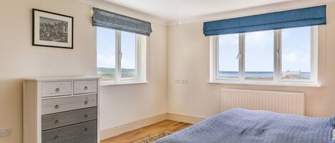 A bedroom with a bed, dresser, two windows with views, and a radiator.