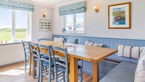 A cozy dining area with a wooden table and chairs, a blue bench, and a view of the outdoors. - Penhallick House (Tintagel)